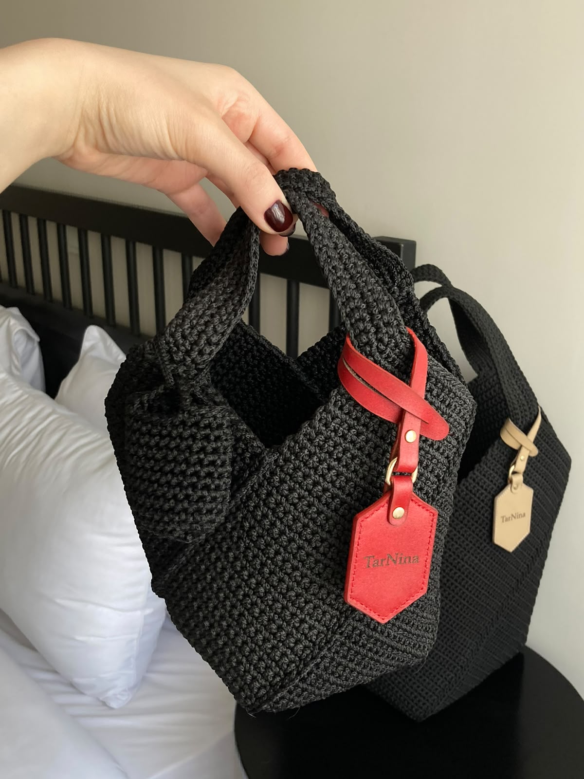 Black TarNina handcrafted crochet bag with a distinctive red leather tag, being lifted by hand