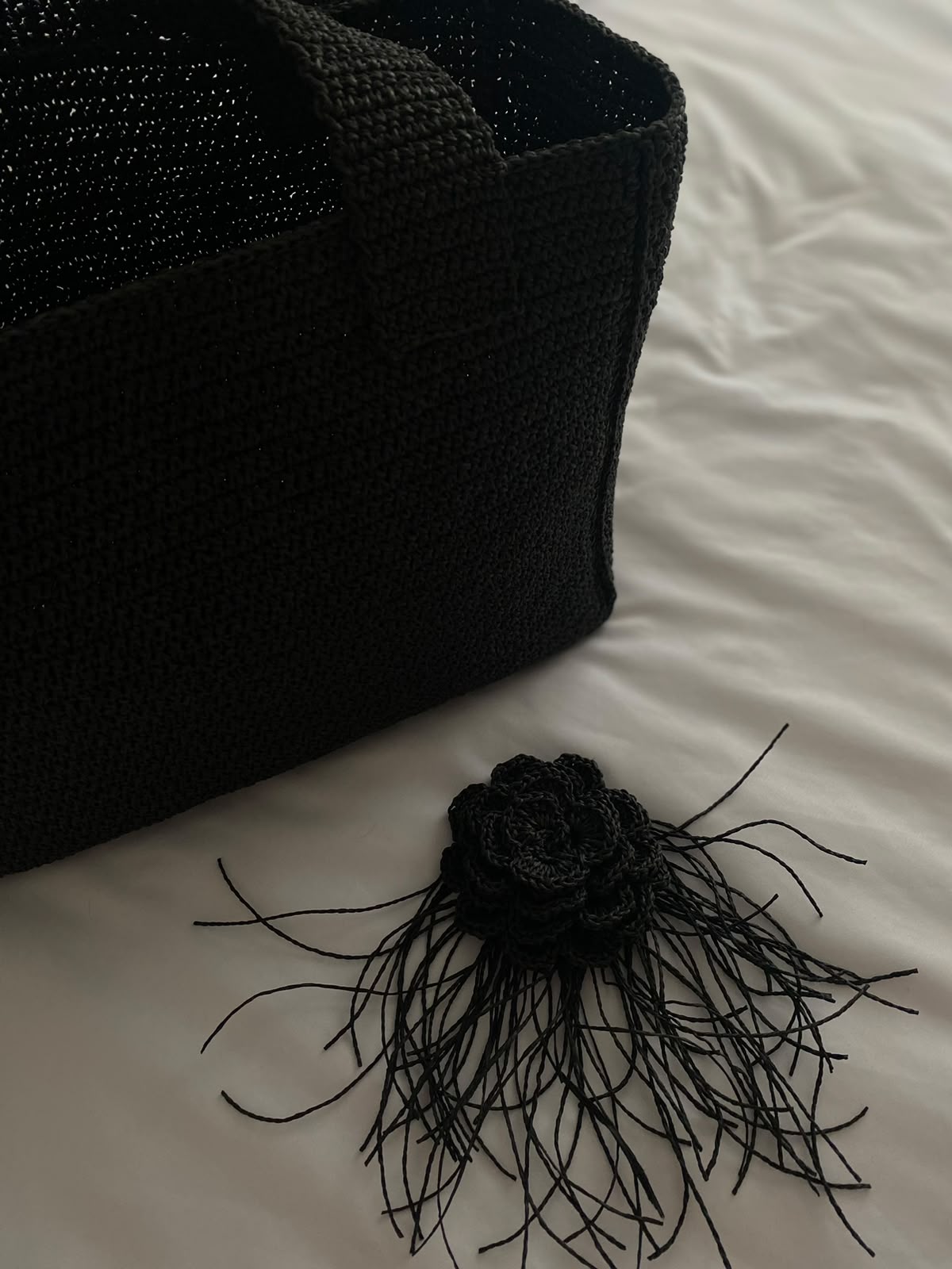 Close-up of a handcrafted TarNina black crochet bag with intricate stitching and a handmade floral ornament with fringe detail — showing the craftsmanship in every piece